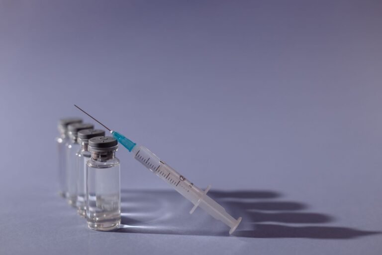 Biologic drug lymphoma risk: unlabeled medicine vials and a syringe on a gray surface, representing injectable biologic drugs