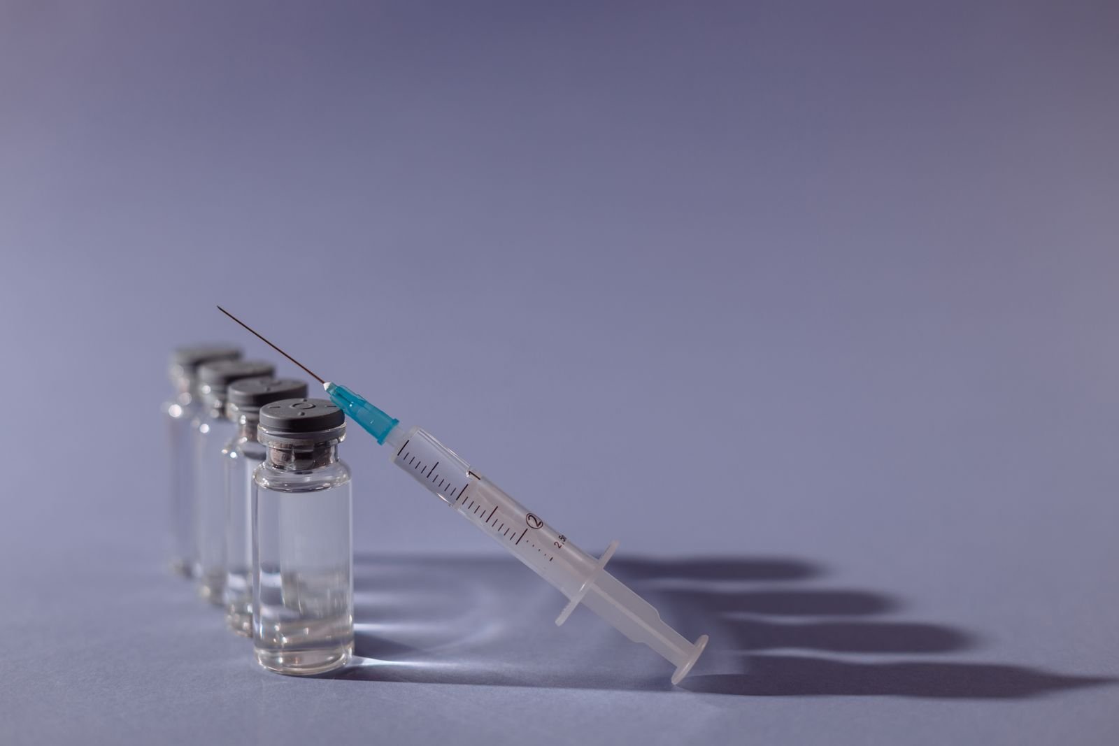 Unlabeled medicine vials and a syringe on a gray surface, representing injectable biologic drugs