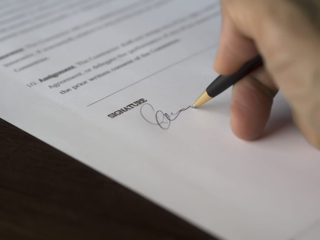 Utility wildfire settlements: close-up of a hand signing a settlement agreement with a pen on a wooden desk