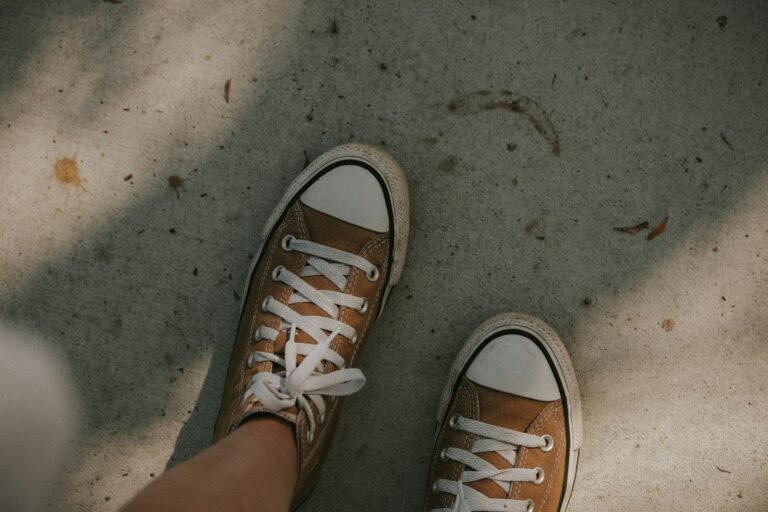 Cartiva toe implant patients: close-up of a person's feet in tennis shoes standing on a sunlit concrete path