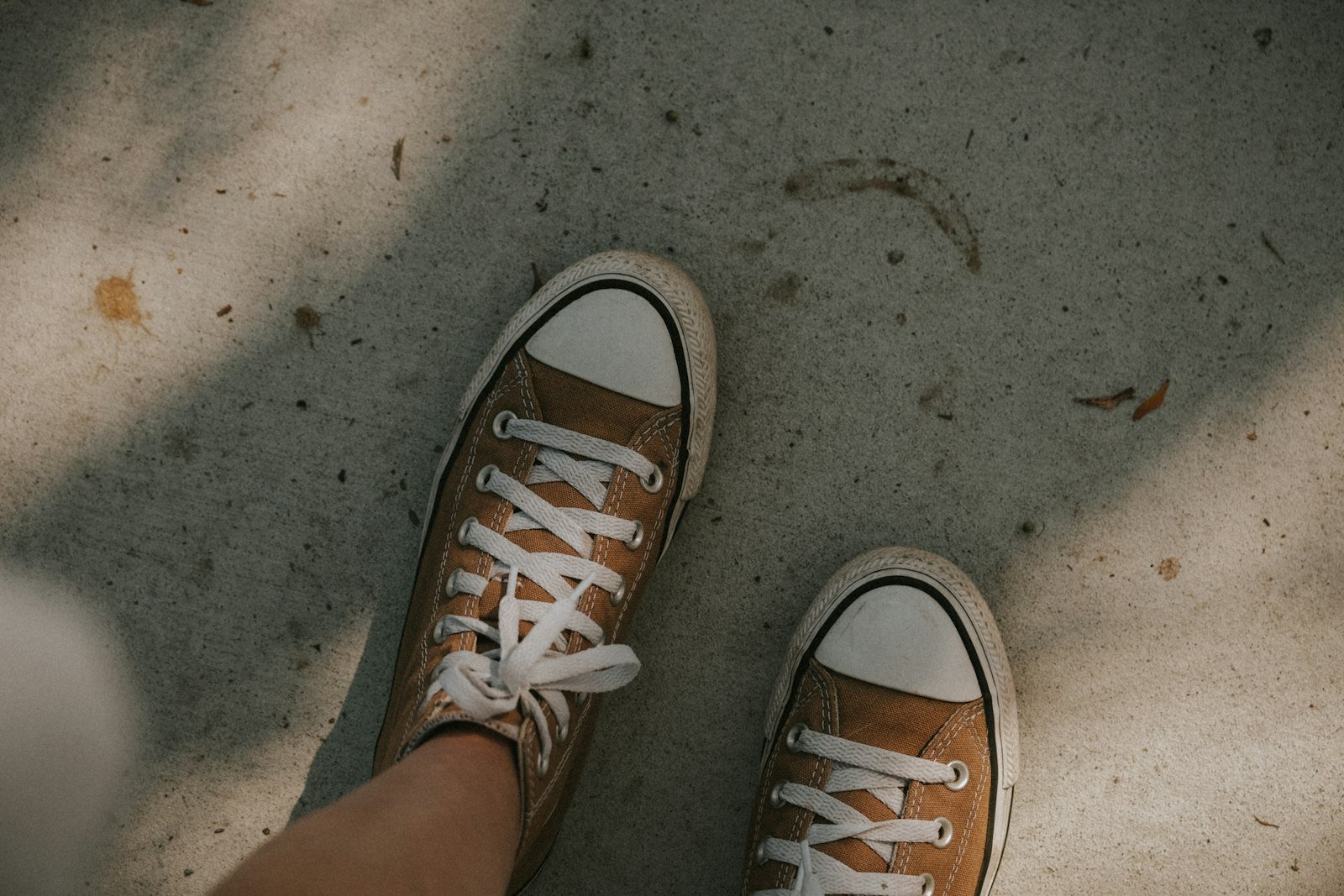 Cartiva toe implant patients: close-up of a person's feet in tennis shoes standing on a sunlit concrete path