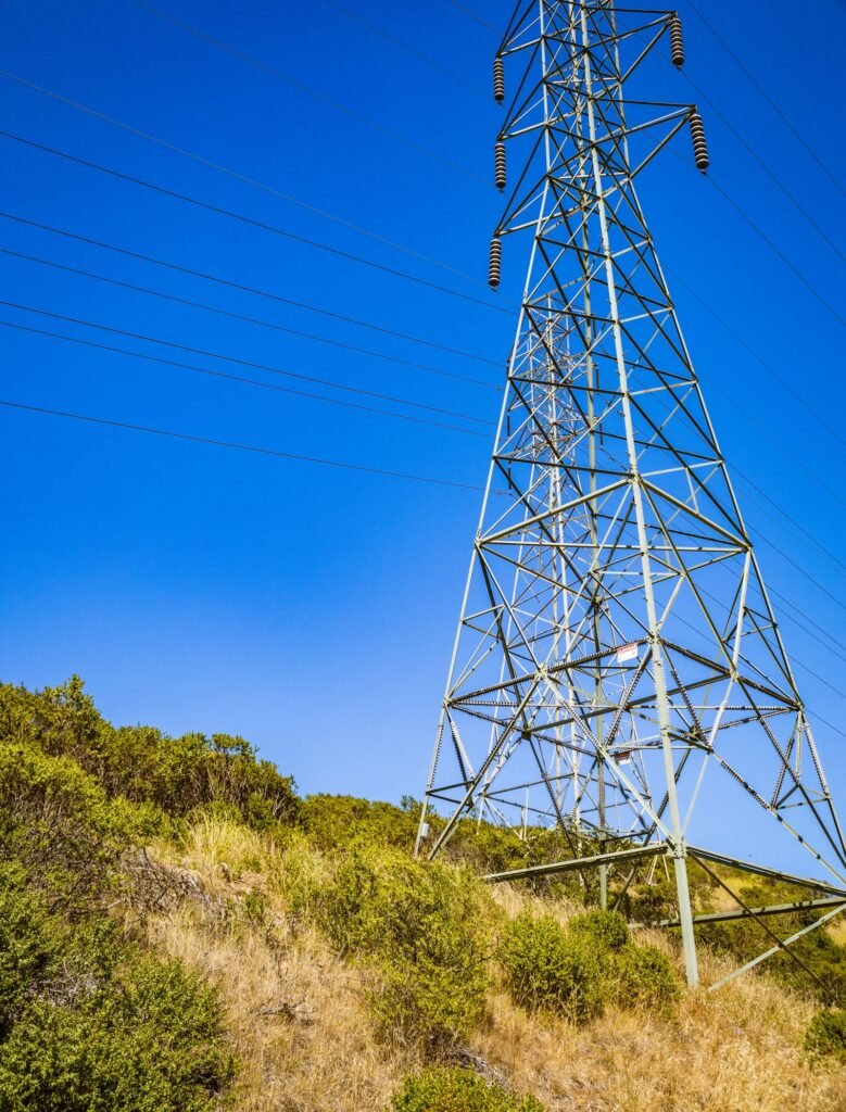 Inverse condemnation: steel electricity pylon beside a dry grassy hillside under a blue sky