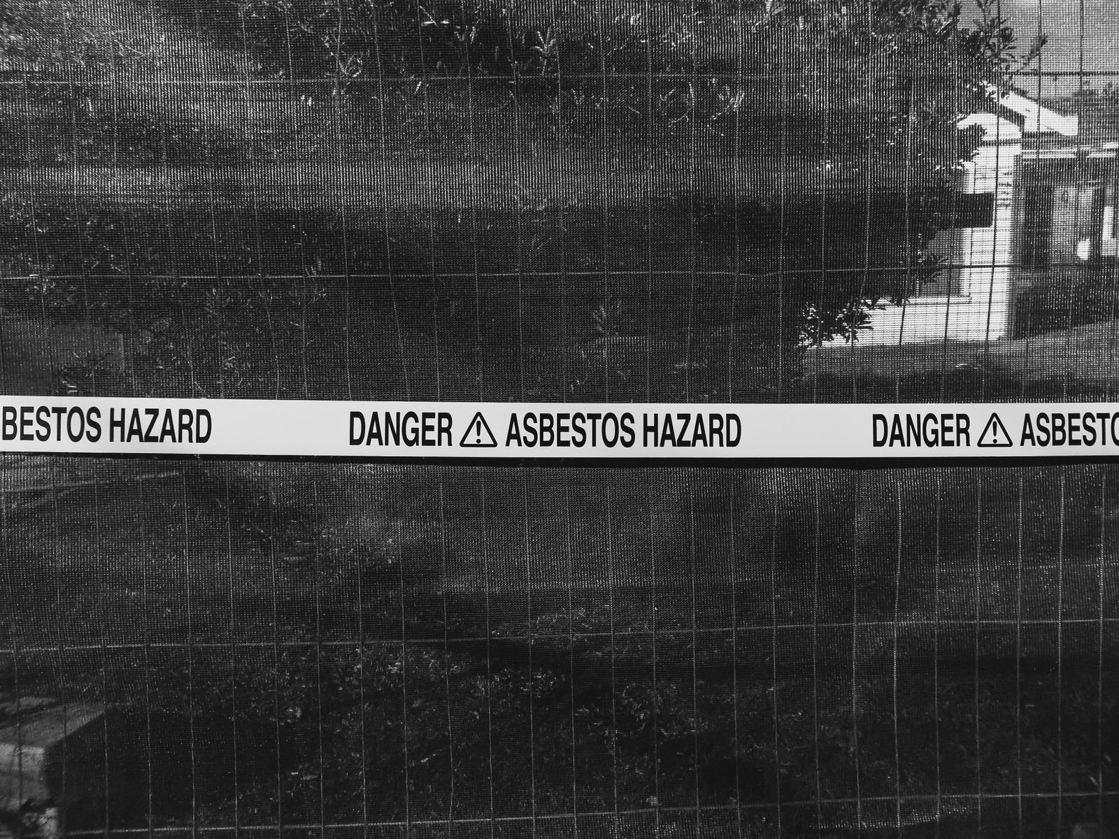 Mesothelioma lawsuit settlements: black and white photo of an asbestos hazard warning sign on a fence