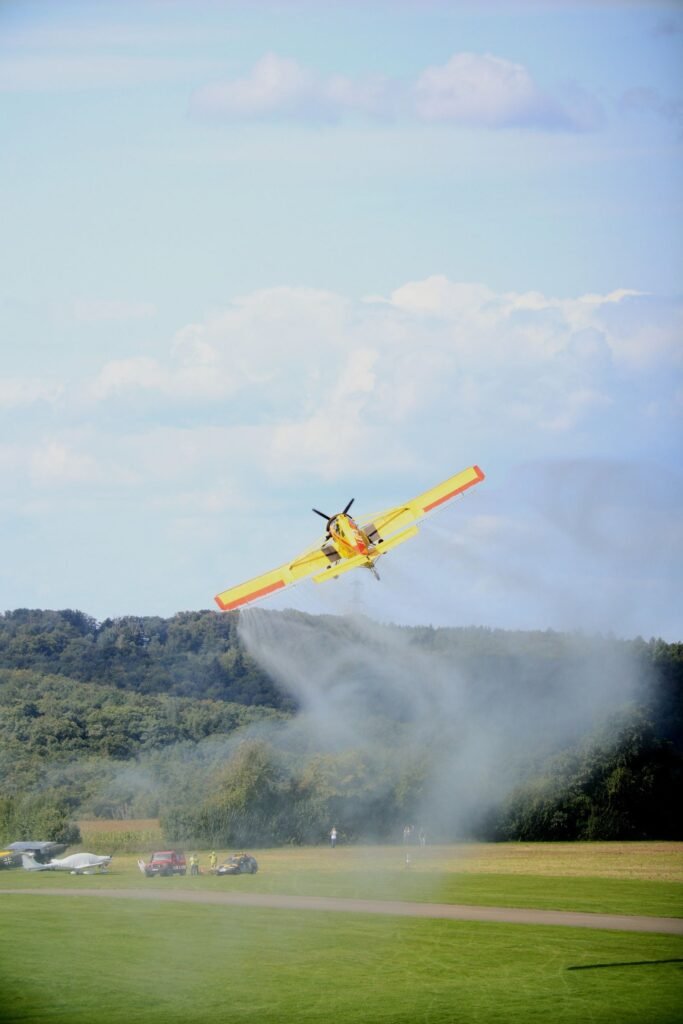Pesticide drift exposure: yellow crop duster plane spraying a green field, leaving a trail of mist