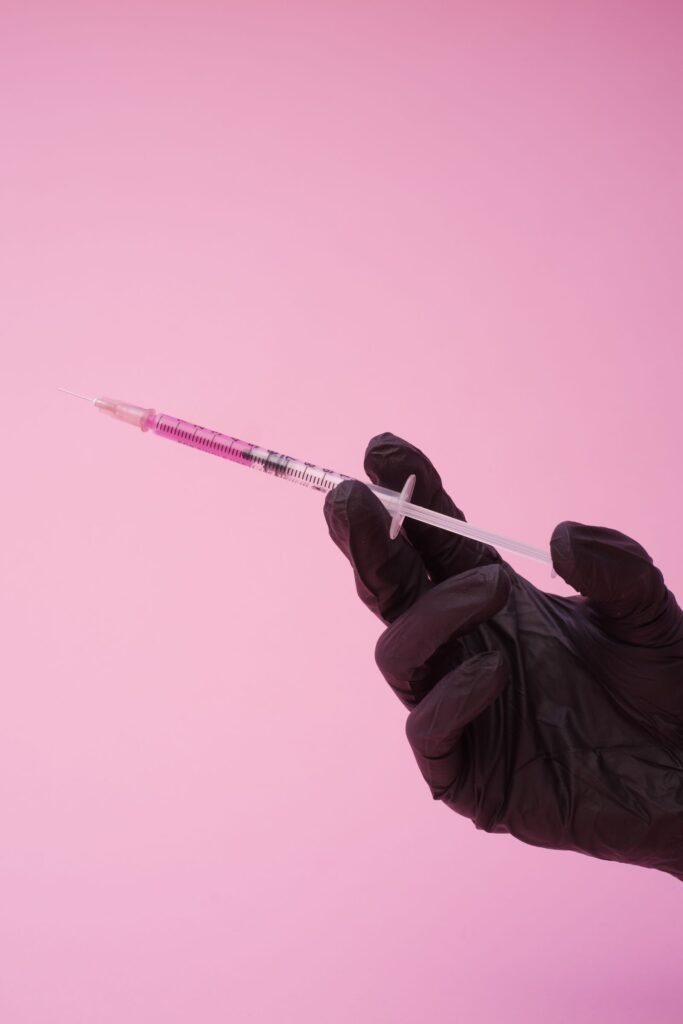Depo-Provera injection records: gloved hand holding a syringe against a pink background