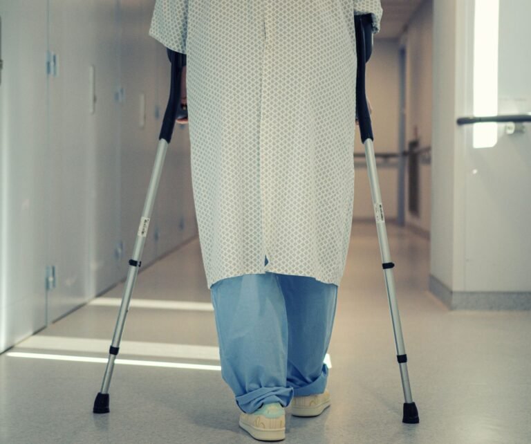 Cartiva implant claims: patient seen from behind walking with crutches down a hospital corridor