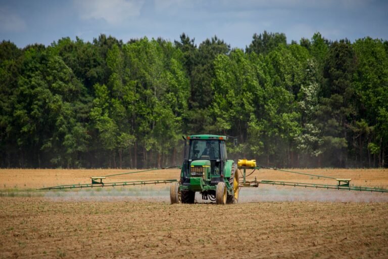 Roundup cancer lawsuit: tractor spraying a green farm field with a forest in the background