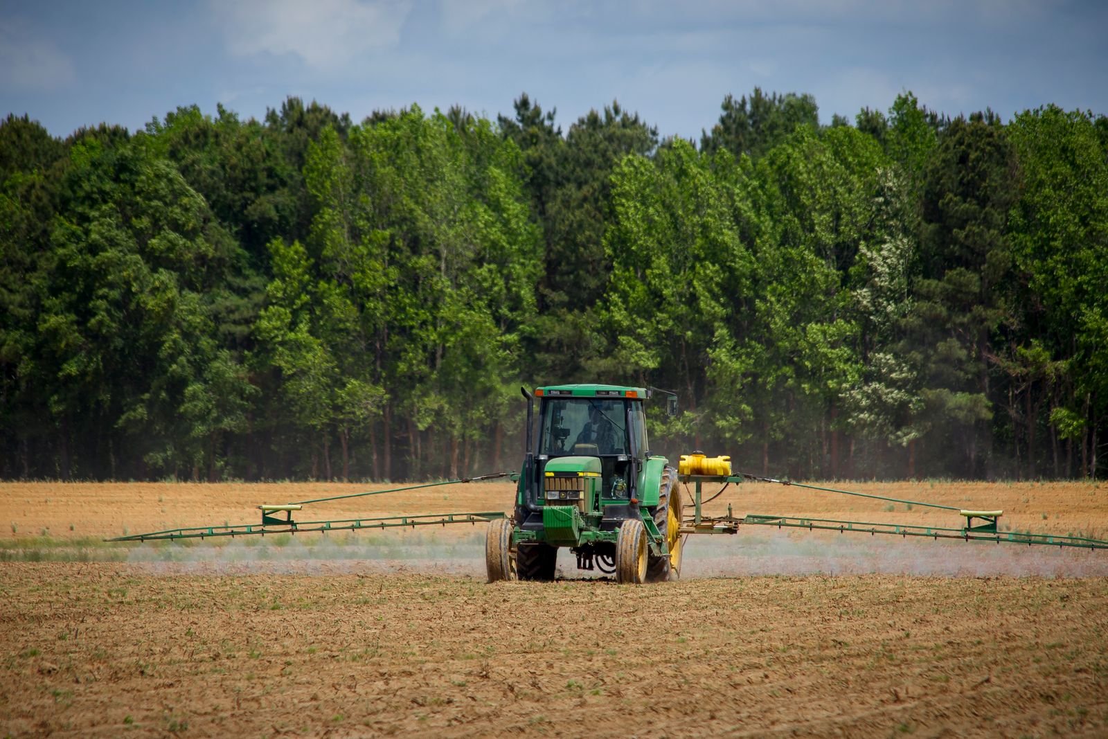 Roundup cancer lawsuit: tractor spraying a green farm field with a forest in the background