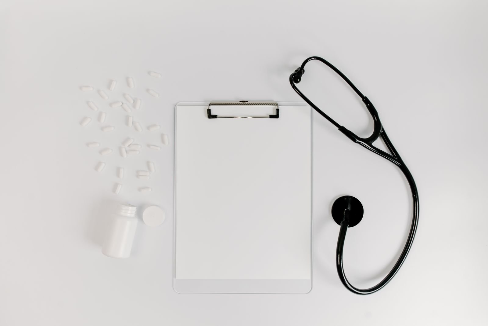 Clipboard with a blank medical form beside a stethoscope and pills, representing medical records