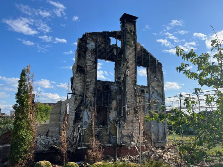 Wildfire loss documentation: ruins of a burned-down house with charred walls under a clear blue sky