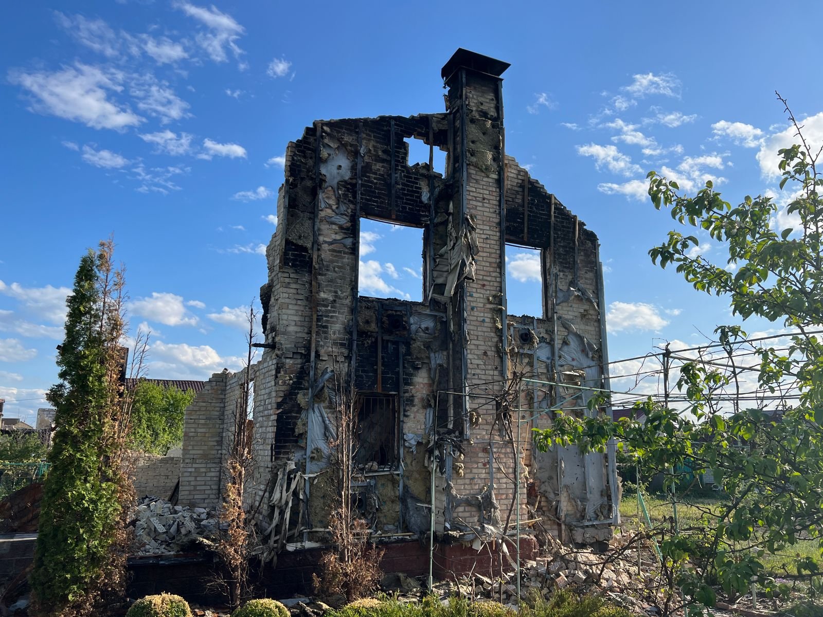Wildfire loss documentation: ruins of a burned-down house with charred walls under a clear blue sky