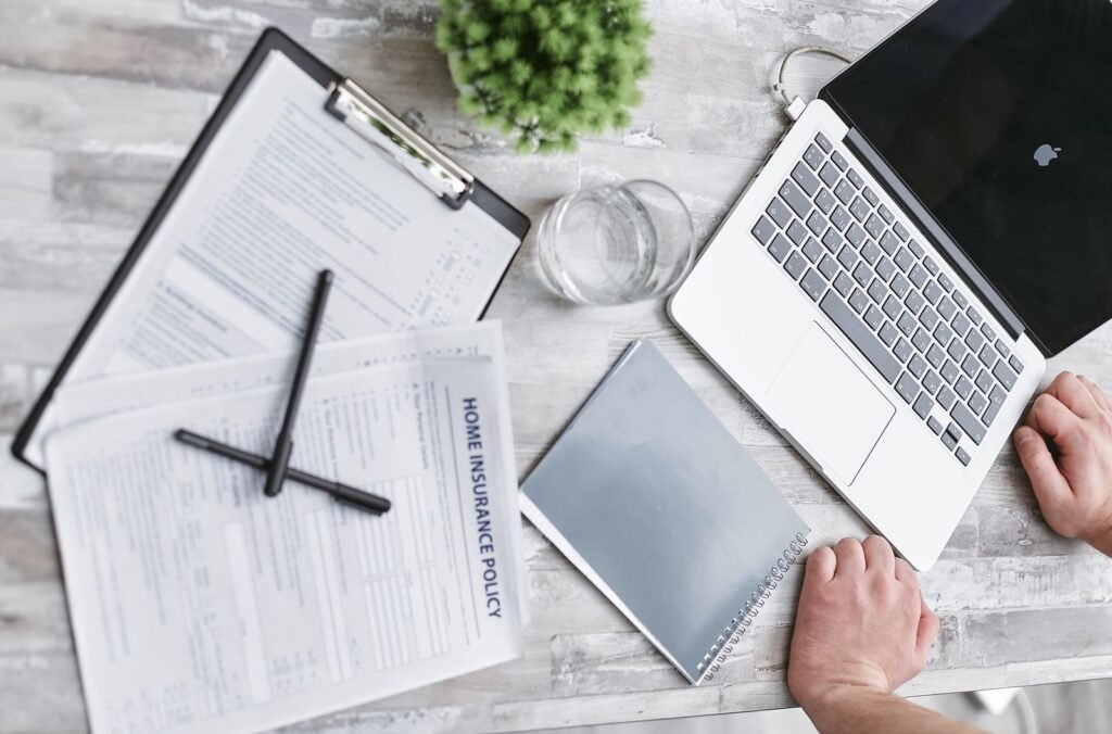 Wildfire loss documentation: hands filling out home insurance forms on a desk beside a laptop