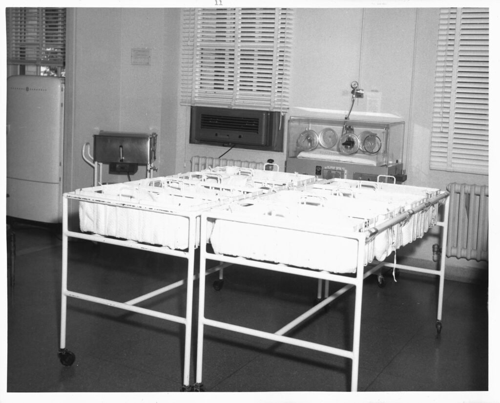 Two empty hospital bassinets on a metal stand in a nursery room