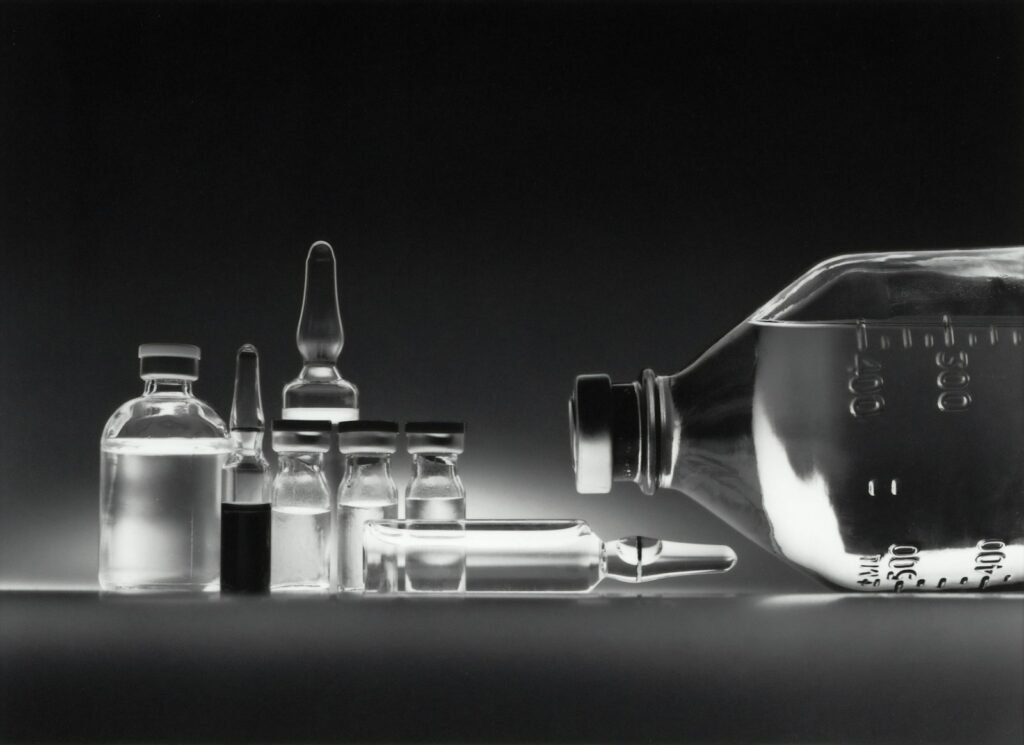 Glass medicine vials and an IV bottle on a dark surface, representing biologic drug lymphoma risk research