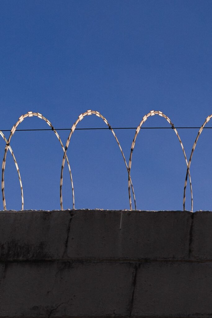 CIW abuse claims: razor wire coiled along the top of a concrete wall under a clear blue sky