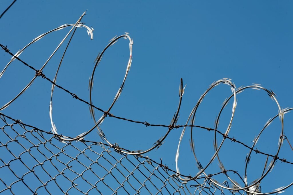 Razor wire on a chain link fence under a blue sky, a reminder of prison settings behind CIW abuse claims