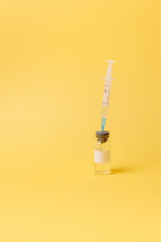 Syringe resting on a small unlabeled medicine vial against a yellow background