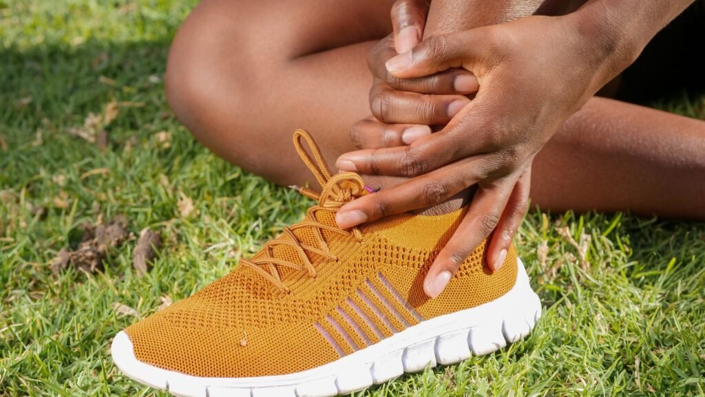 Person sitting on grass and holding a sore ankle and foot while wearing a running shoe