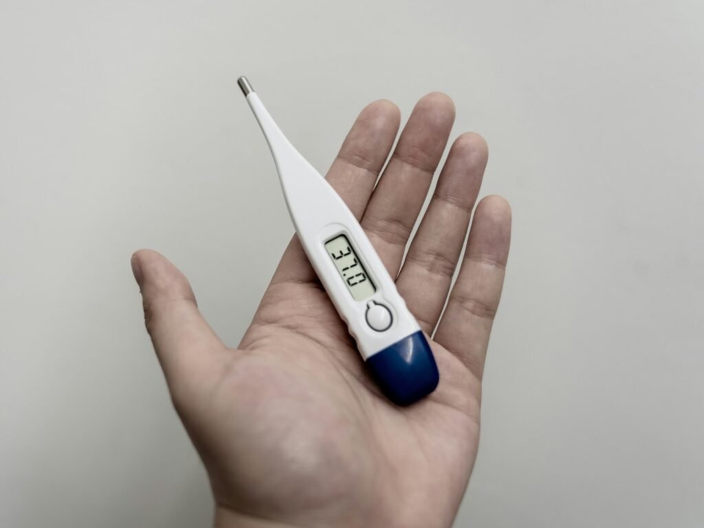 Hand holding a digital thermometer showing a temperature reading, used to check for fever