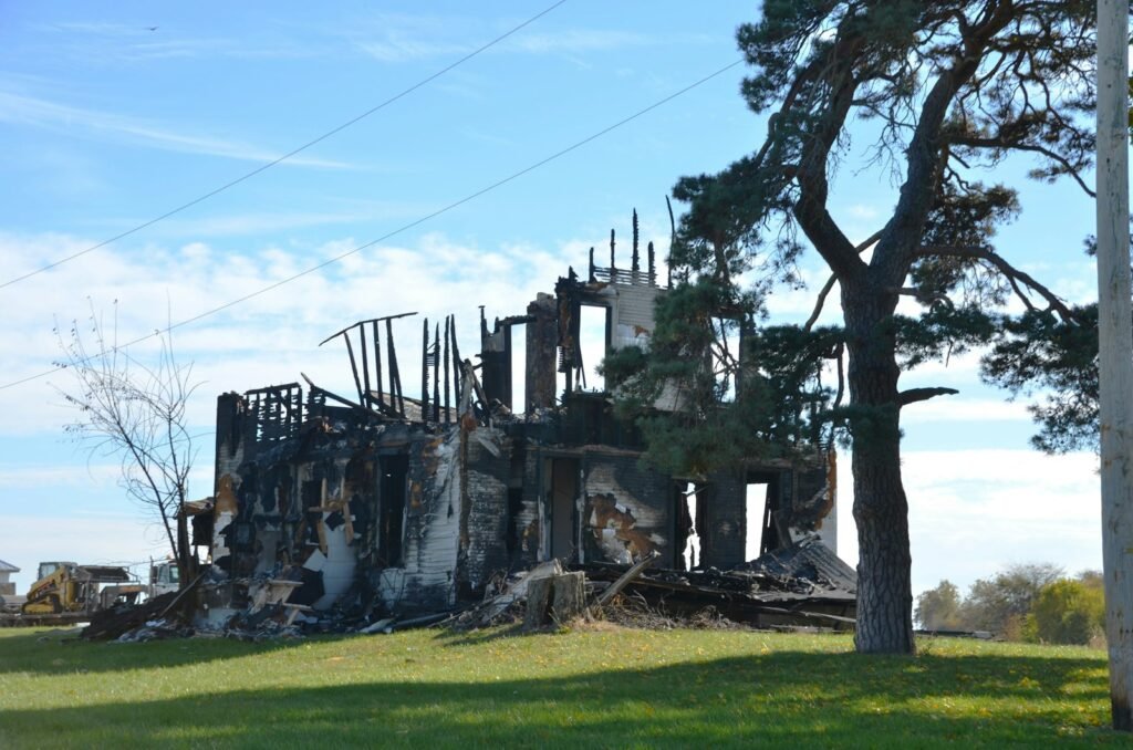 Burned-out house with charred remains beside a lone tree after a fire