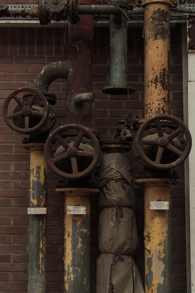 Rusty old pipes and valves on a brick wall, the kind of setting reviewed under mesothelioma evidence standards
