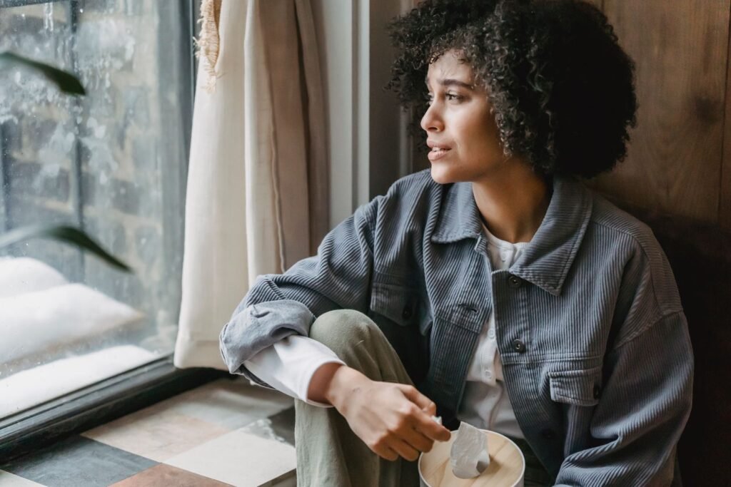 Woman sitting by a window, reflecting, illustrating survivors weighing an institutional abuse claim