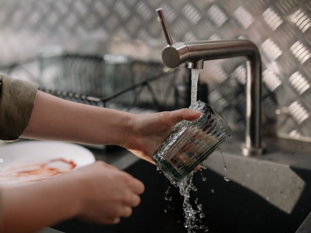 Hands rinsing a glass under running tap water, a reminder of drinking water at issue in PFAS lawsuits