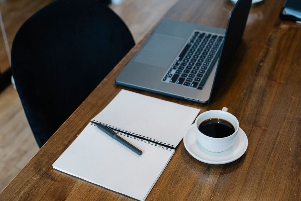 Laptop and spiral notebook on a wooden table with coffee, a quiet setup for reviewing a fee agreement
