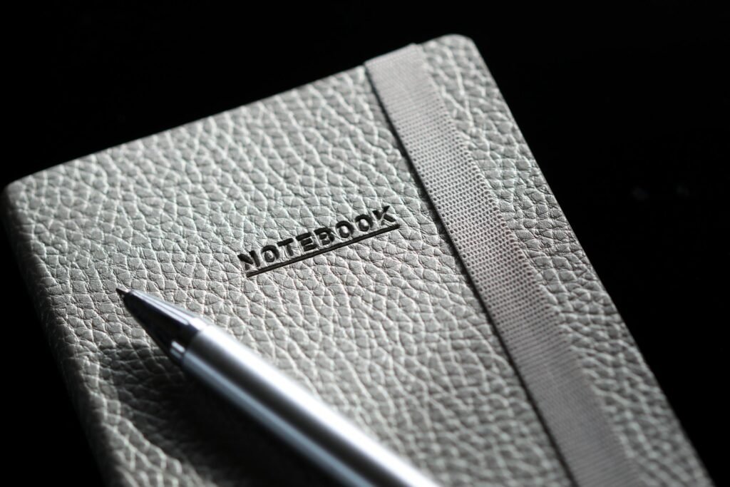 Close-up of a computer keyboard beside a notebook and pen on a desk