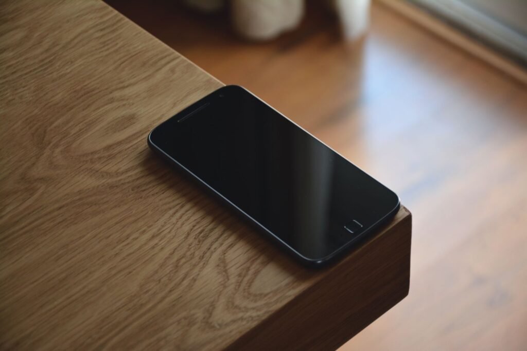 Black smartphone resting on the edge of a wooden table in warm light