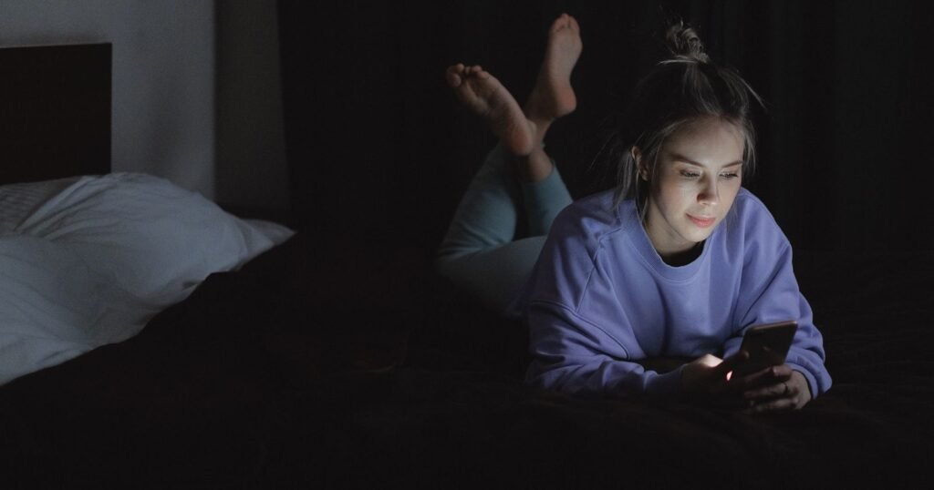 Teenager scrolling social media on a phone in bed at night