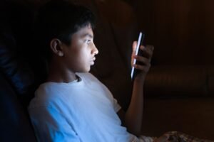 Teenager using a smartphone late at night, lit by the screen glow, illustrating social media addiction