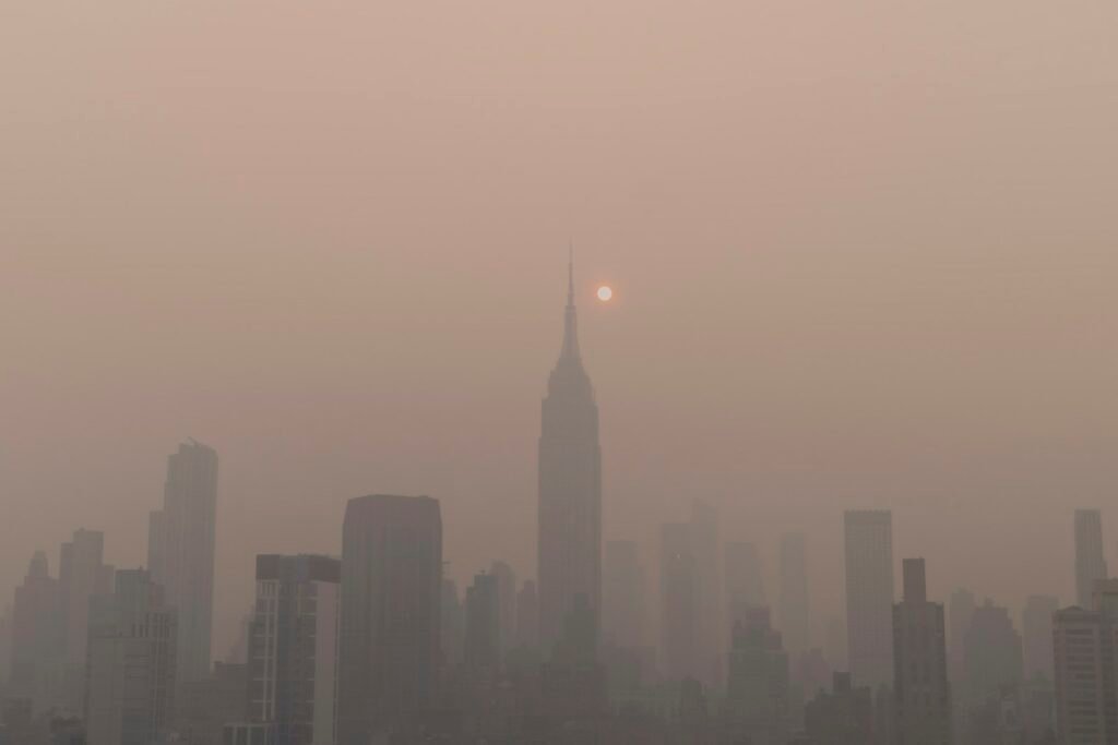City skyline hidden behind thick haze and smoke, with the sun glowing faintly in the distance