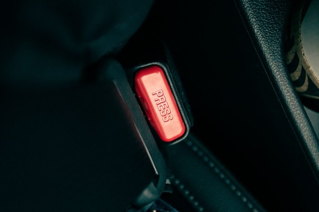 Close-up of a car seat belt buckle with a red release button, a simple safety step for back-seat riders