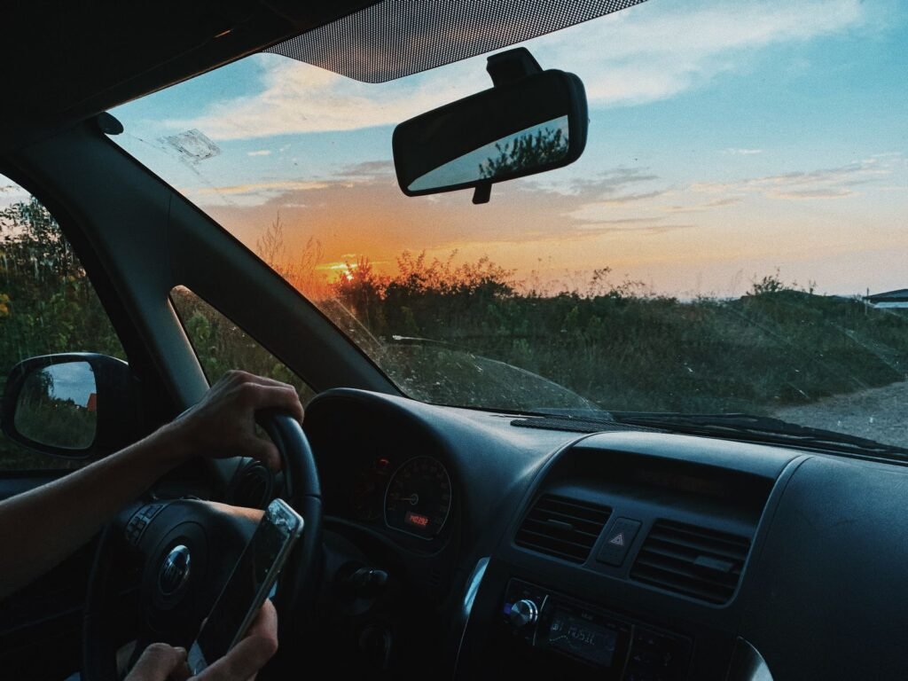 Faceless driver holding a smartphone on a rural road at sunset, a behavior linked to distracted driving deaths