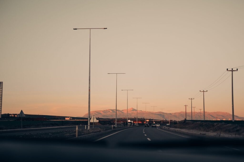 Empty highway lined with lampposts at dusk with mountains in the background