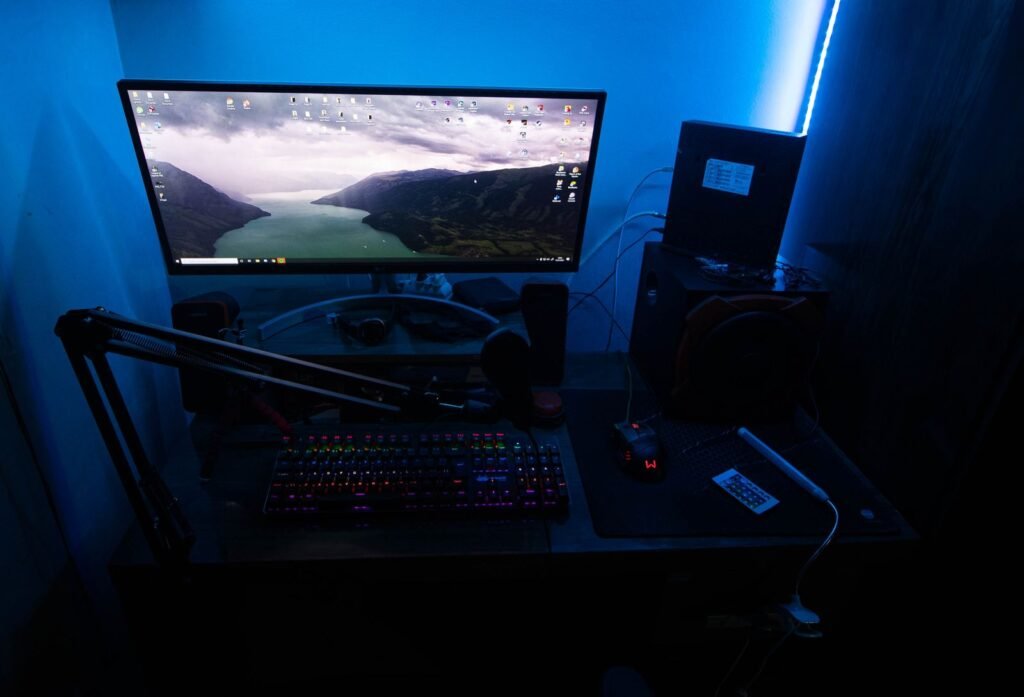 Gaming desk with a monitor and keyboard glowing under blue light in a dark room