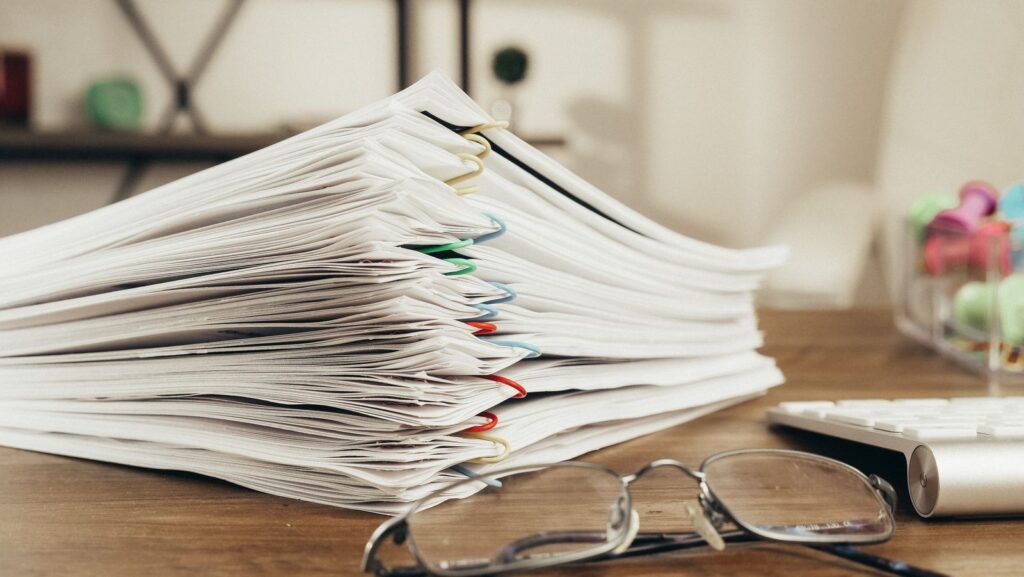 Stack of paper-clipped documents and eyeglasses on a desk, showing organized records and reports